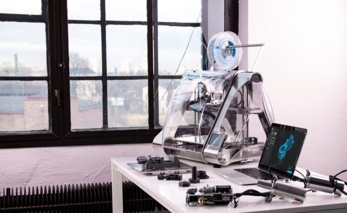 A 3D printer next to a laptop and some prototypes
